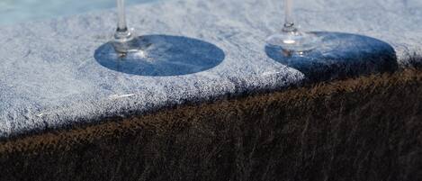 Two glasses of water with floating items on a stone ledge by a pool.