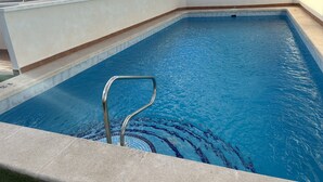Una piscina rettangolare con una scala in metallo, circondata da un solarium piastrellato.