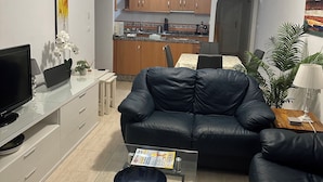 Un soggiorno con un divano in pelle nera, un tavolino in vetro, una televisione a schermo piatto e una ventola a soffitto.