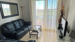 Un soggiorno con un divano in pelle nera, un tavolino in vetro, una televisione a schermo piatto e un vaso decorativo con fiori.