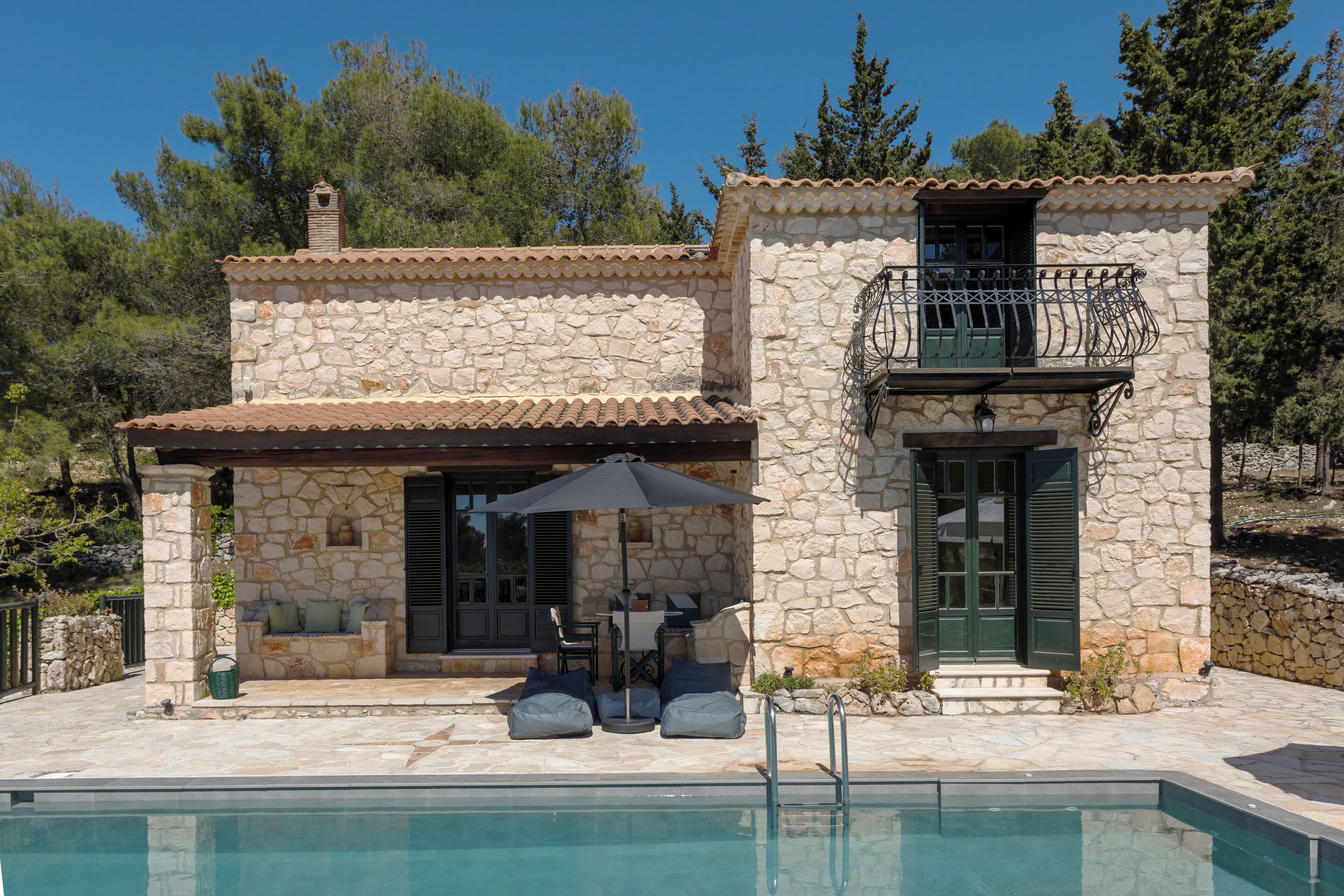 A stone house with a pool, outdoor seating, and a balcony.