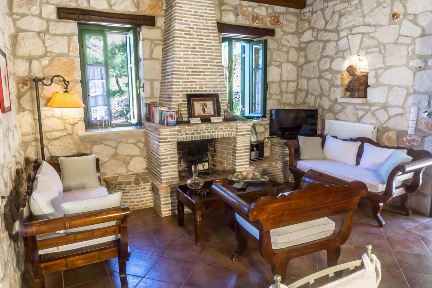 Un salón con paredes de piedra, una chimenea, un sofá, una silla y un televisor.