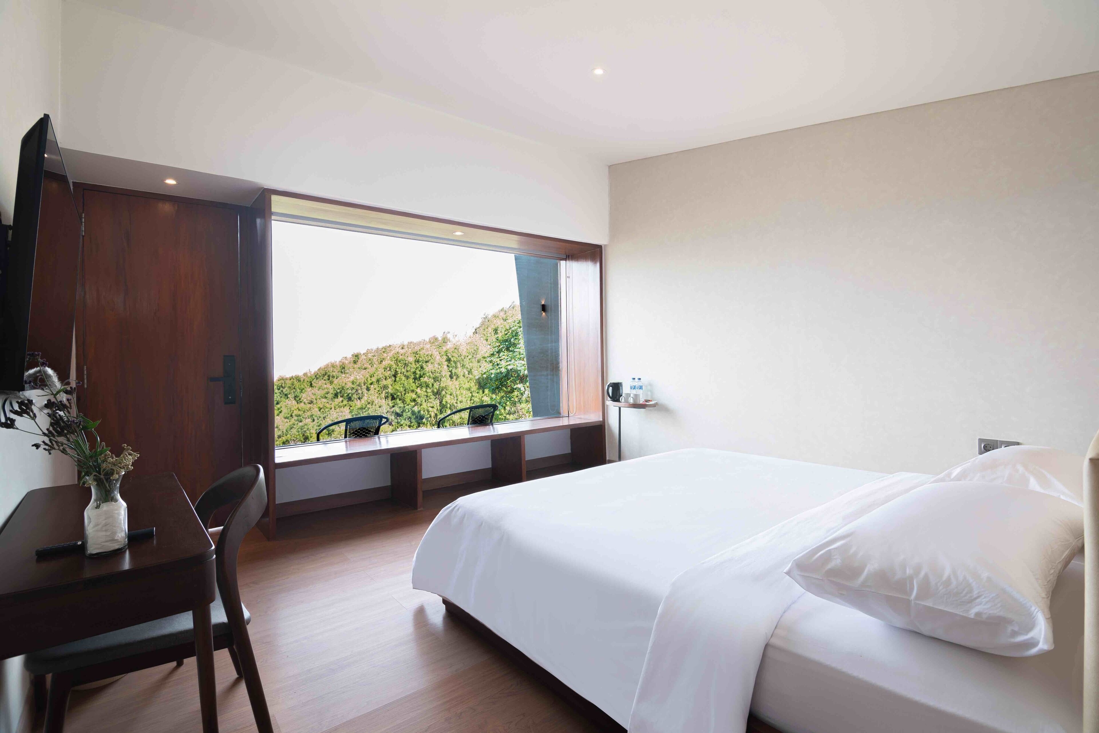 A bedroom with a large window, a bed, a desk, and a chair.