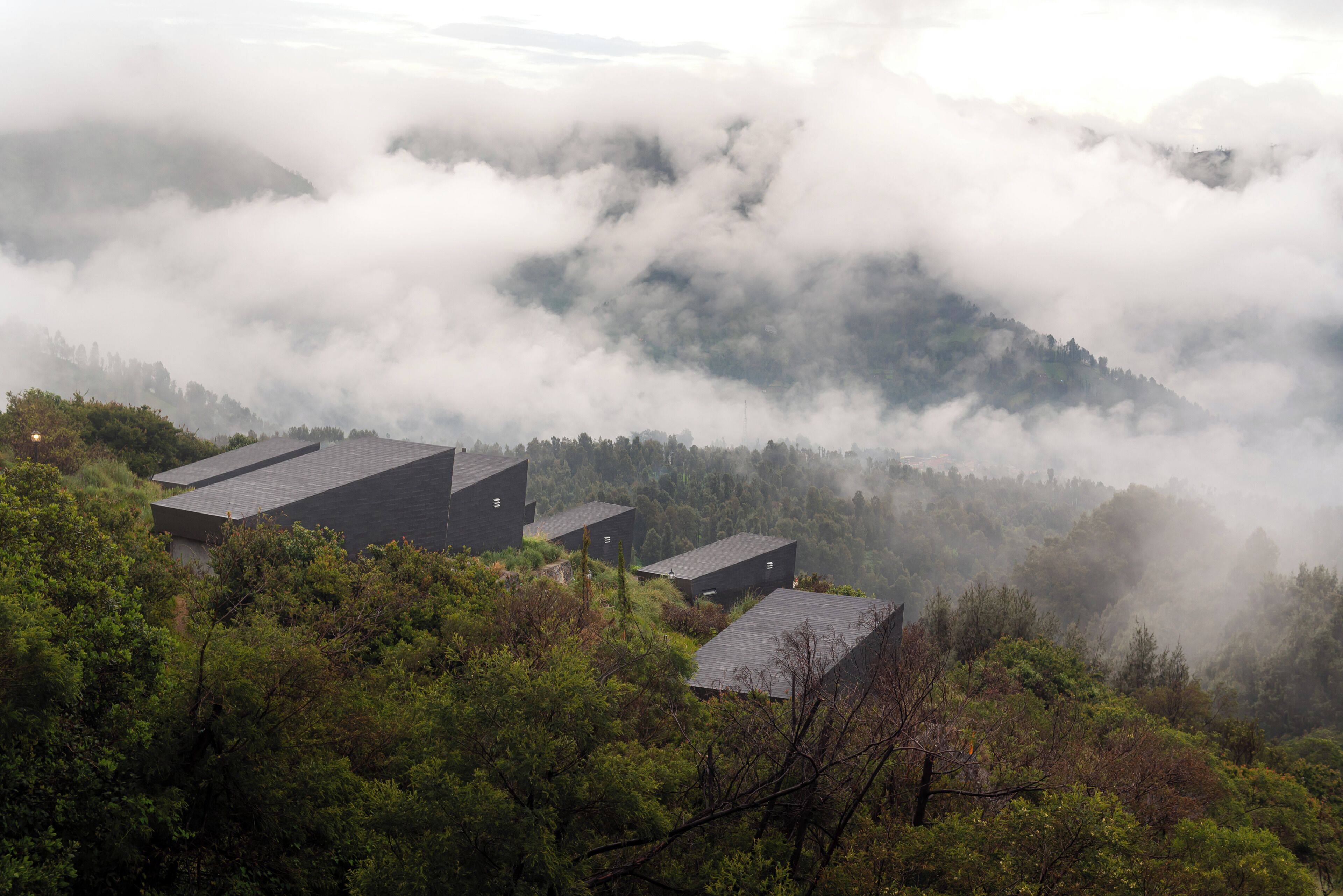 A mountainous landscape with several buildings surrounded by dense forest and enveloped in fog.