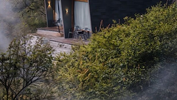 A secluded cabin with a small deck, two seating areas, and a view of the surrounding forest. - ARTOTEL Cabin Bromo (Ngadisari)