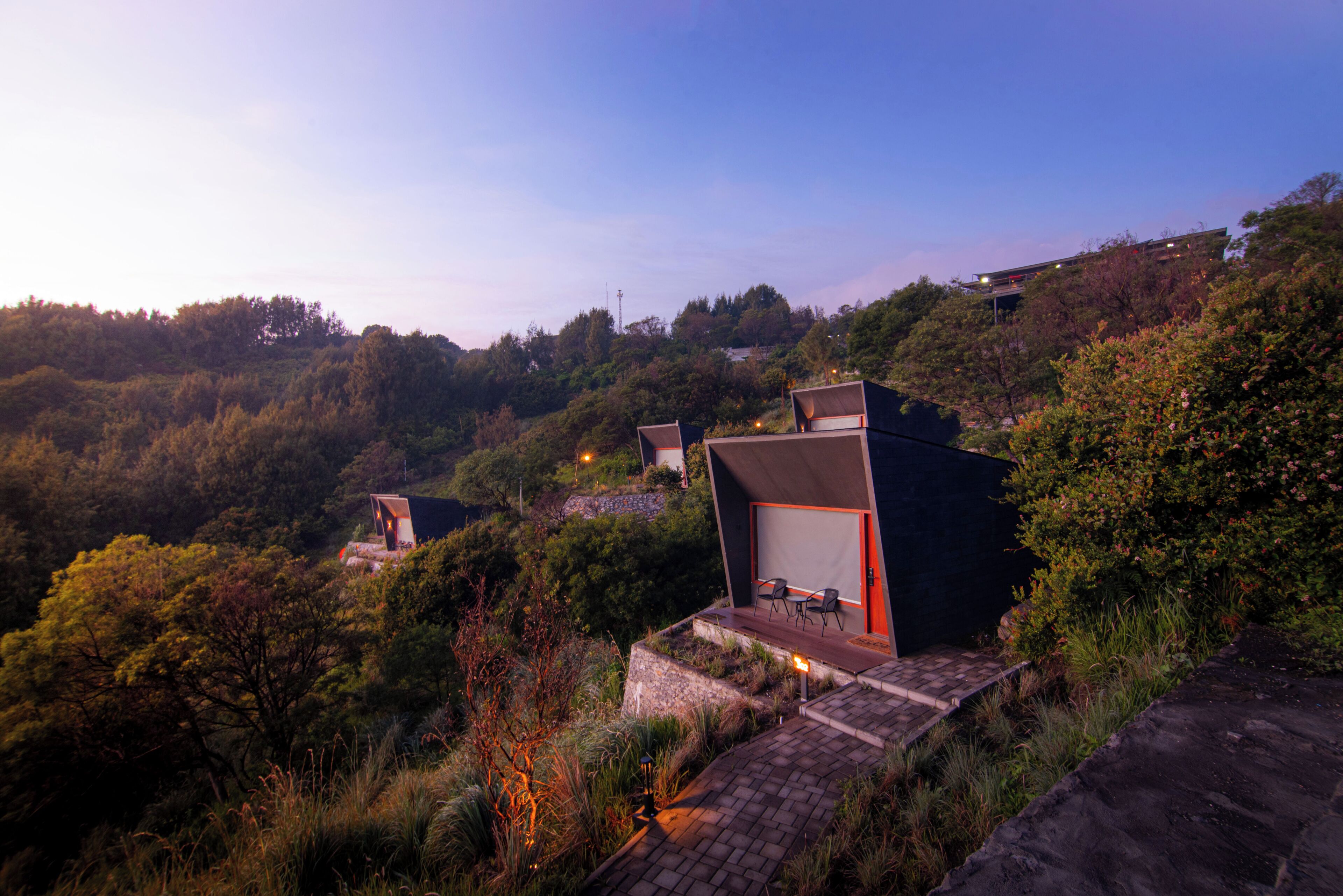 A modern building with a flat roof, surrounded by dense vegetation and hills.