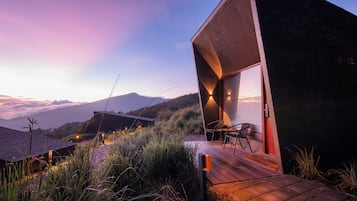 Un edificio moderno con entrada de vidrio, terraza de madera y vistas a montañas.