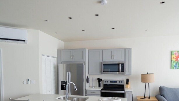 A compact kitchen with grey cabinets, a central island with seating, and a microwave. - Dutch Caribbean Residence B (Oranjestad)