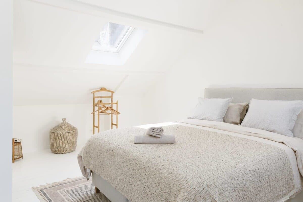 A bedroom with a skylight, a bed with a rolled towel, a hanging chair, and a woven basket.