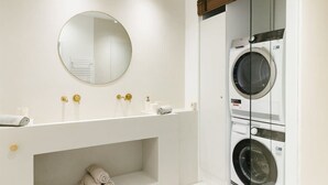 A modern bathroom with a white vanity, a round mirror, gold faucets, and a built-in washing machine. - 3-BR Apartment in Prime Antwerp Location (Antwerpen)