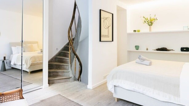 A modern bedroom with a large bed, a glass partition, a wooden staircase, and a minimalist decor. - 3-BR Apartment in Prime Antwerp Location (Antwerpen)