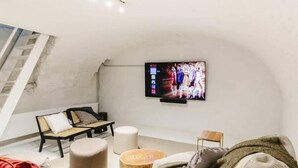 A modern living room with a flat-screen TV mounted on the wall, a black sofa, a wooden stool, and a small wooden table. - 3-BR Apartment in Prime Antwerp Location (Antwerpen)