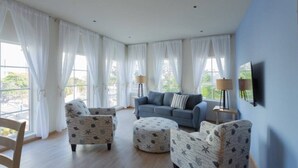 A living room with a blue sofa, patterned armchairs, and ottomans. - Dutch Caribbean Residence E (Aruba Beach Club)