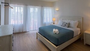 A bedroom with a bed, bedside tables, a hanging coat rack, and sheer curtains. - Dutch Caribbean Residence E (Aruba Beach Club)