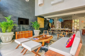 A spacious indoor area with a round wooden coffee table, cushioned seating, and large potted plants.