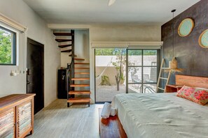 Une chambre à coucher avec un lit, une commode en bois, un escalier et une vue sur l’extérieur.