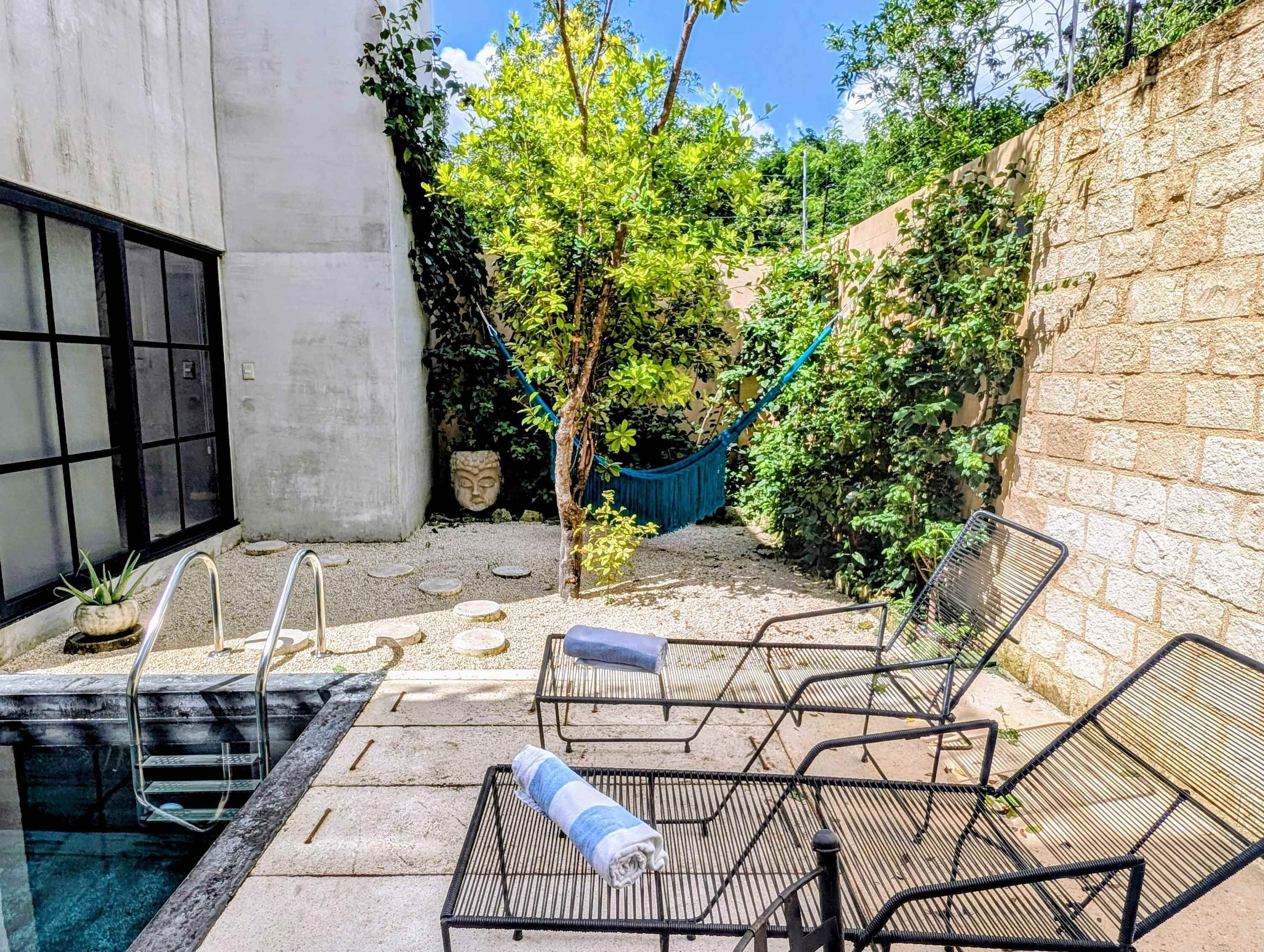 A pool area with a hammock, lounge chairs, and a stone wall.