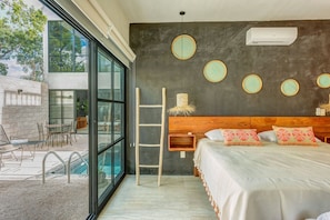 A bedroom with a large window, a bed, a wooden headboard, and a wall-mounted air conditioner.