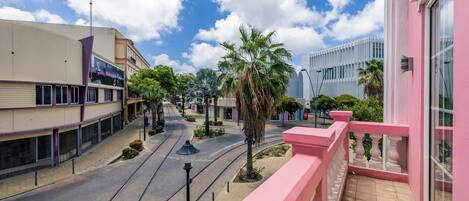 A street view with a pink building, a tram line, and palm trees.