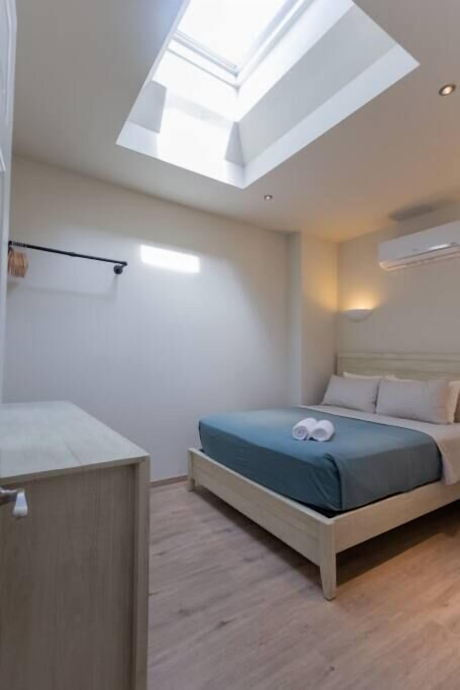 A modern bedroom with a skylight, a bed with a blue bedspread, and a bedside table.