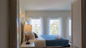 A bedroom with a bed, bedside table, lamp, and windows. - Dutch Caribbean Residence D (Oranjestad)