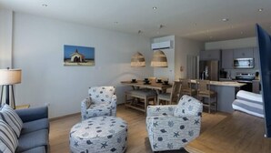 A modern living room with a sofa, two patterned armchairs, a round ottoman, a dining area with a table and chairs, and a kitchen with a microwave and stove. - Dutch Caribbean Residence D (Oranjestad)