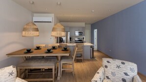 A modern kitchen with a central island, a dining area with a wooden table and chairs, and a blue accent wall. - Dutch Caribbean Residence D (Oranjestad)