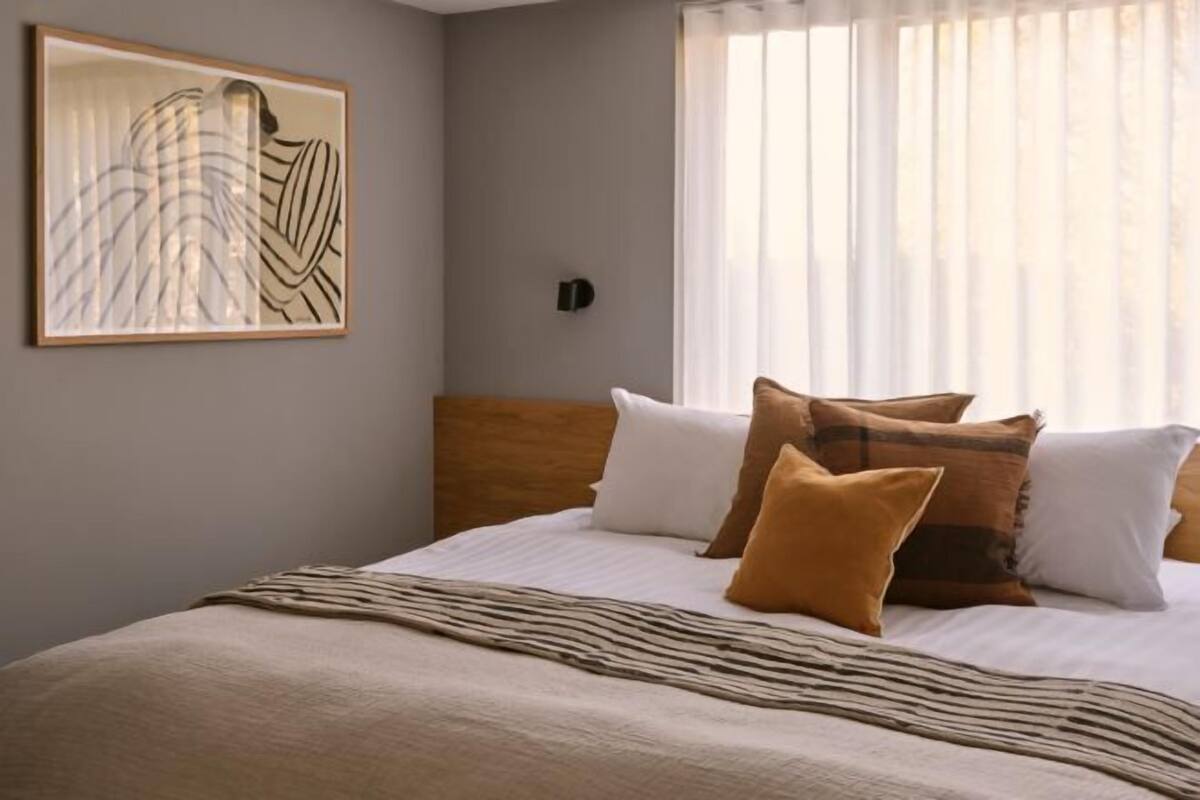 A bedroom with a bed, pillows, a blanket, a wall-mounted light, and a window with curtains.