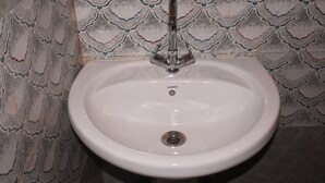 Un lavabo blanc, doté d’un seul robinet, est installé sur un mur recouvert de carreaux décoratifs.