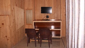 Une pièce aux murs lambrissés, avec un téléviseur posé sur un meuble en bois, deux chaises en bois et un rideau sur le côté droit.