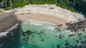 An aerial view of a beach with clear turquoise waters, a sandy shore, and rocky outcrops.