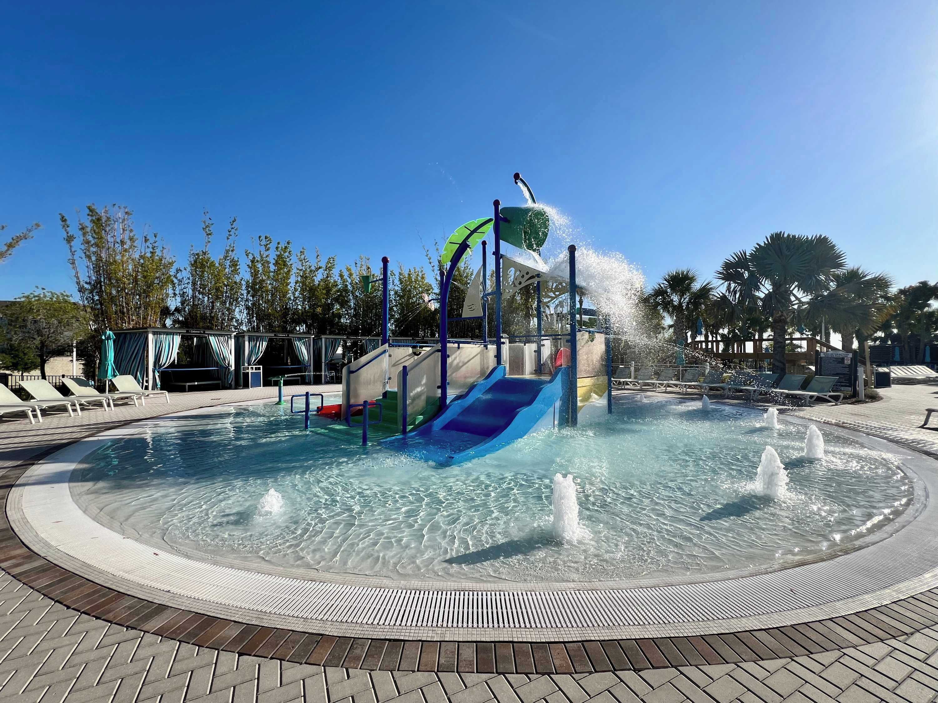 A water park with a central water slide, a hot tub, and a pool area with lounge chairs.