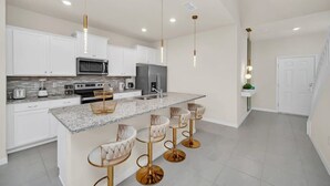 A modern kitchen with white cabinets, a granite countertop, and gold bar stools.
