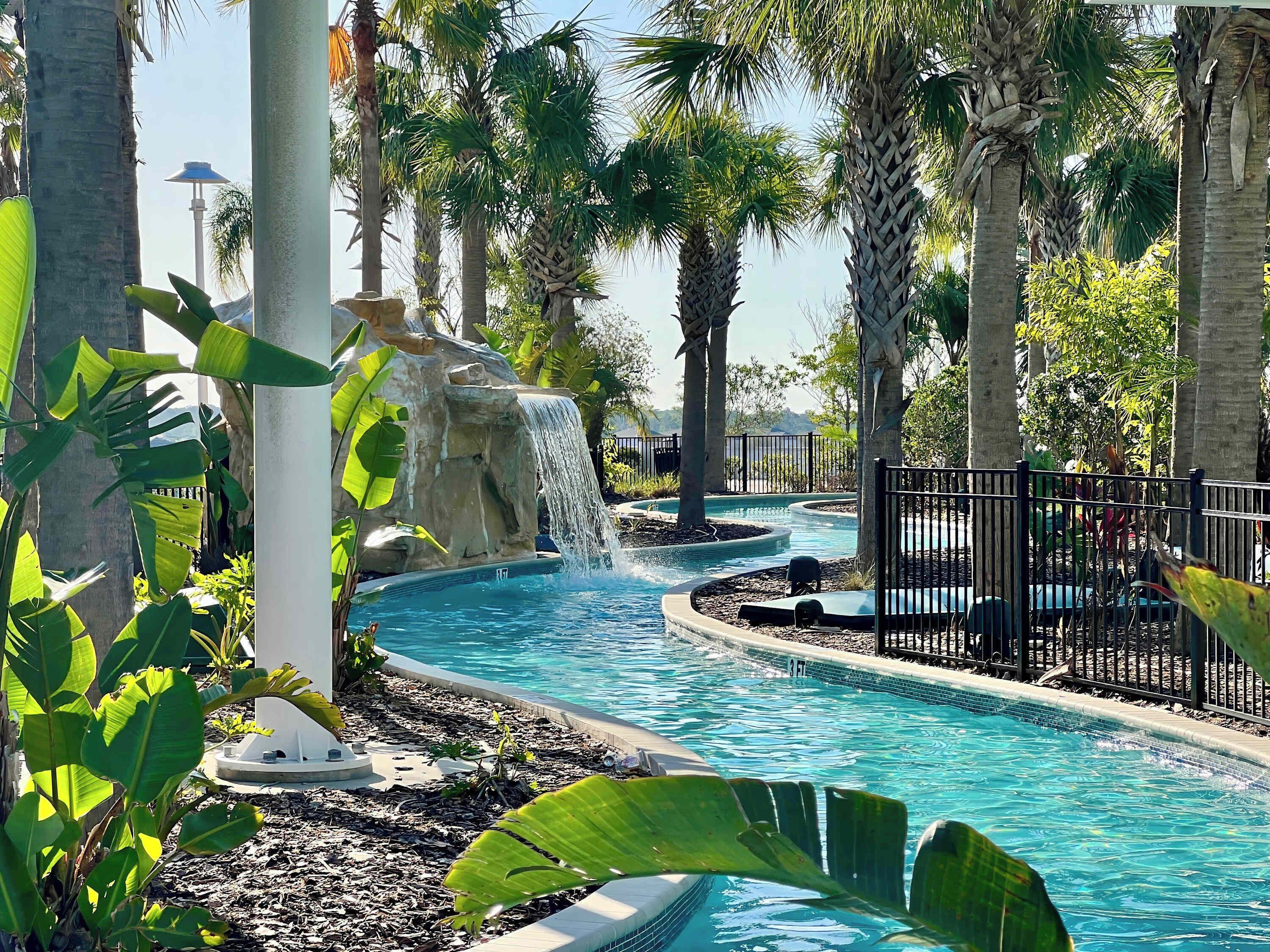 Un espace piscine agrémenté d’une cascade, entouré de palmiers et de plantes tropicales.