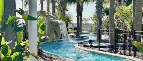 Un área de piscina con una cascada, rodeada de palmeras y plantas tropicales.