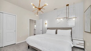 A bedroom with a large bed, a nightstand, a modern chandelier, and a marble wall.