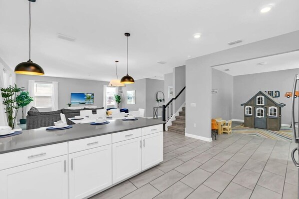 A modern kitchen with white cabinets, a grey countertop, and pendant lighting. - Mickey | Minions | Game Room | 6 Miles Disney 4569 (Kissimmee)