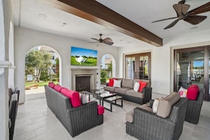 A spacious living area with wicker furniture, a fireplace, and large windows offering views of the outdoors. - Desert Hideaway: 2BR/2BA, BBQ, FirePit, PGA West! (La Quinta)