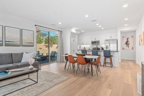 A modern living room with a sofa, coffee table, and a dining area with chairs and a table.