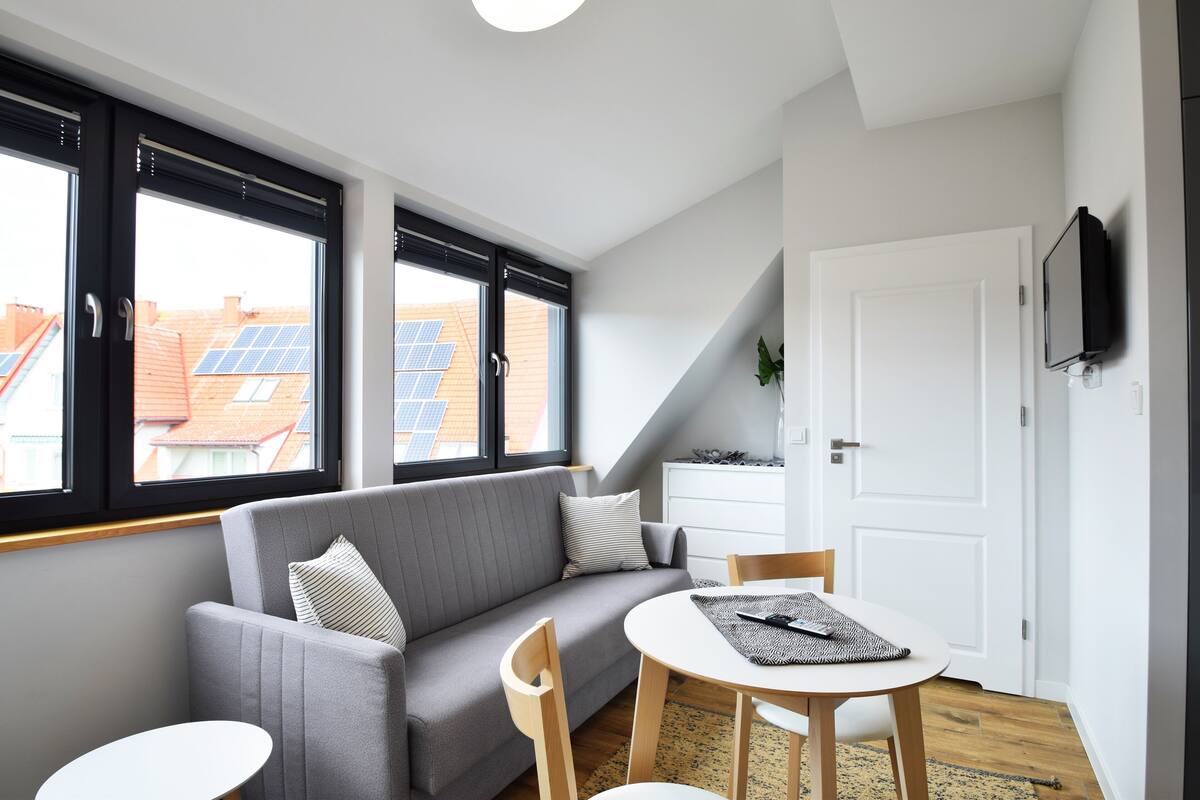 A modern living room with a grey sofa, a round table, and a TV mounted on the wall.