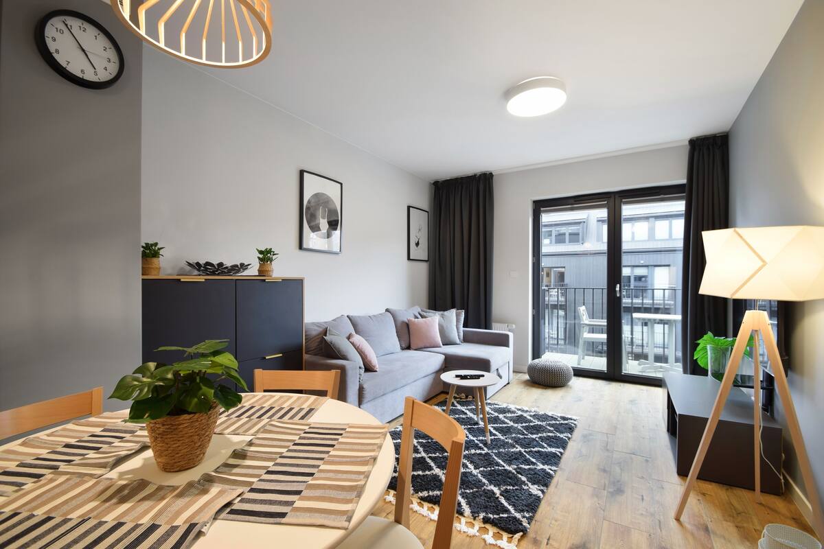 A modern living room with a dining table, sofa, and a view of the city through large windows.
