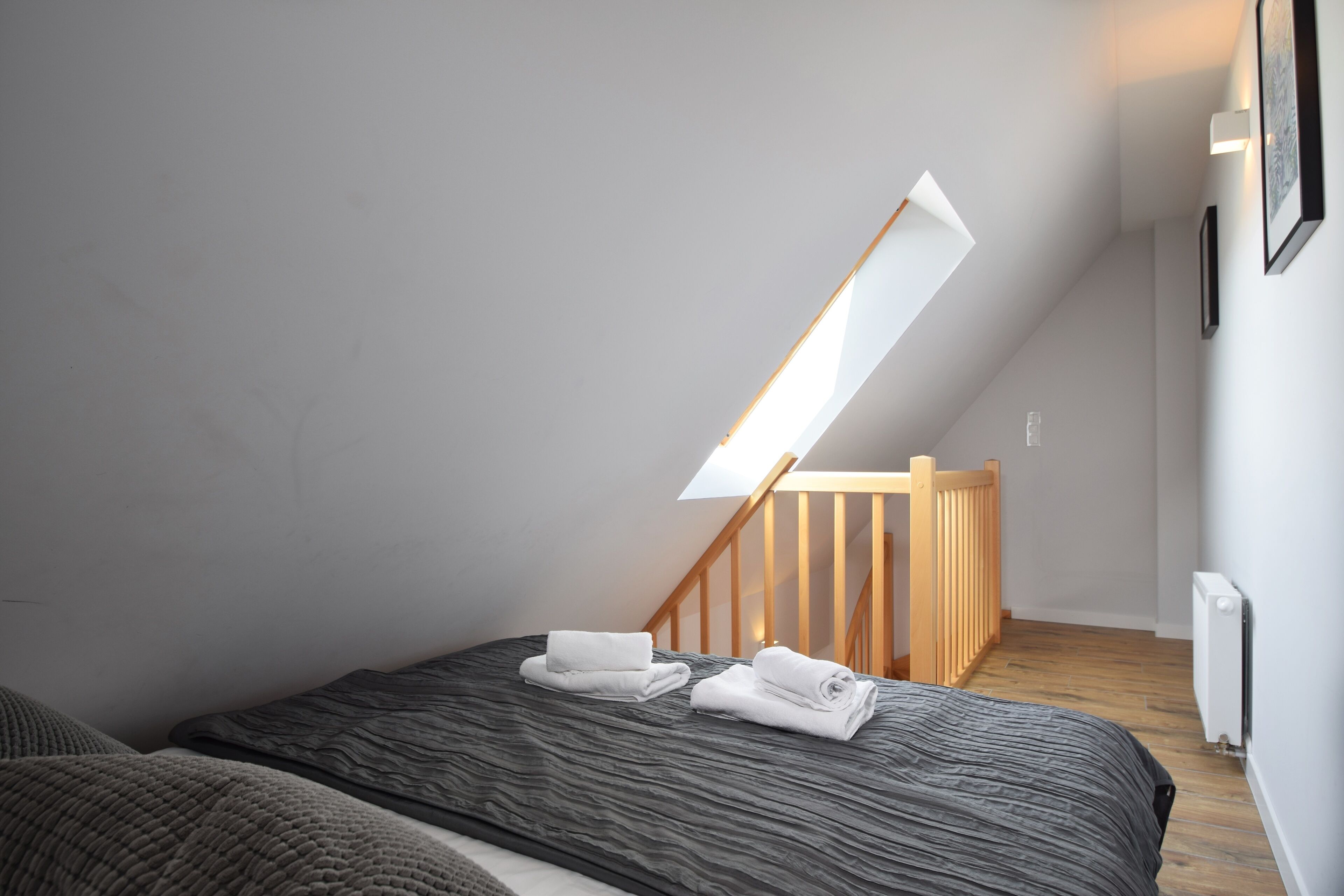 Une chambre moderne avec un plafond en pente, un puits de lumière, un escalier en bois et des serviettes soigneusement pliées sur le lit.