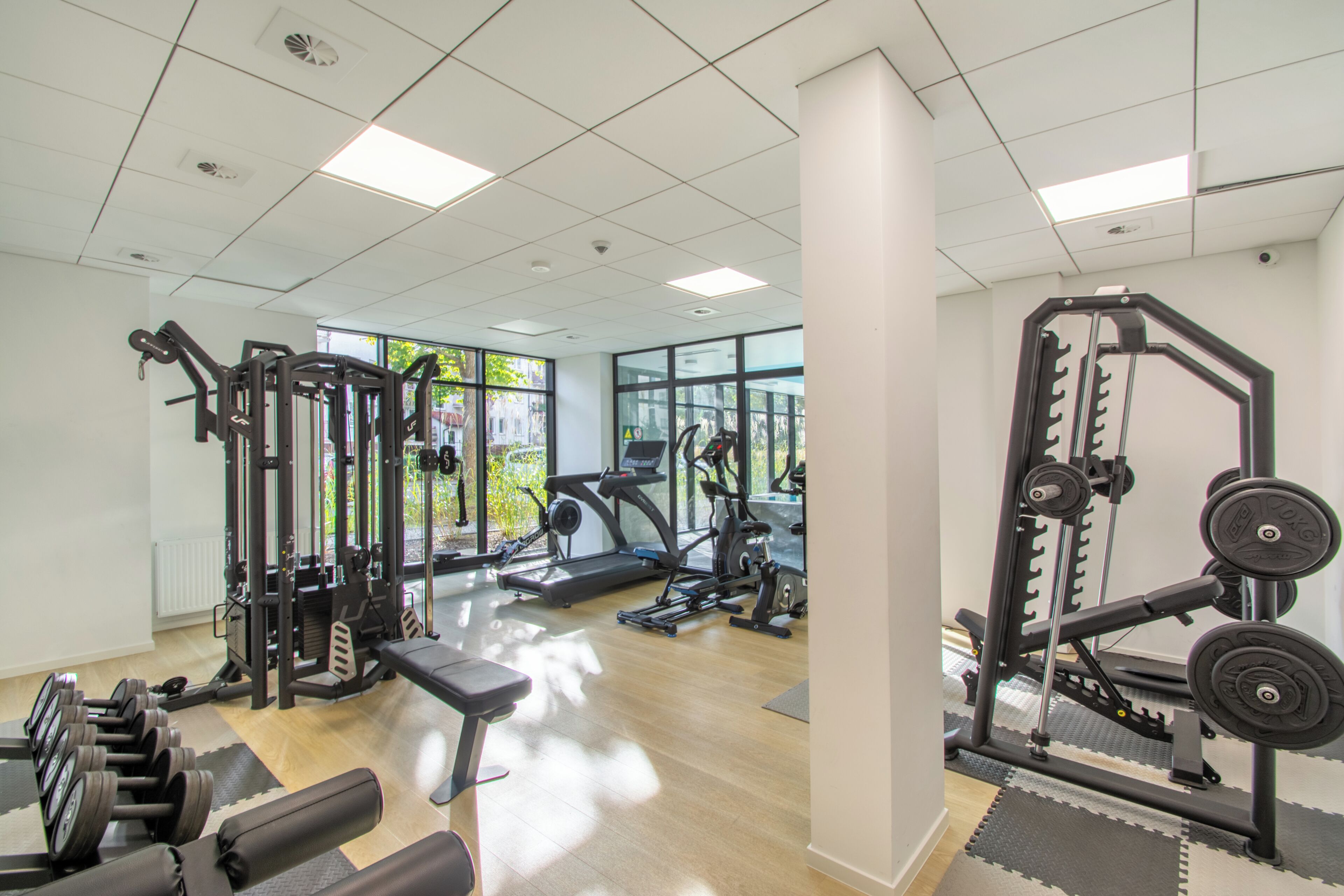 Een fitnessruimte met trainingsapparatuur, grote ramen en een schoon, modern design.