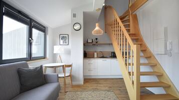 Una sala de estar moderna con un sofá gris, una escalera de madera y una zona de cocina al fondo.