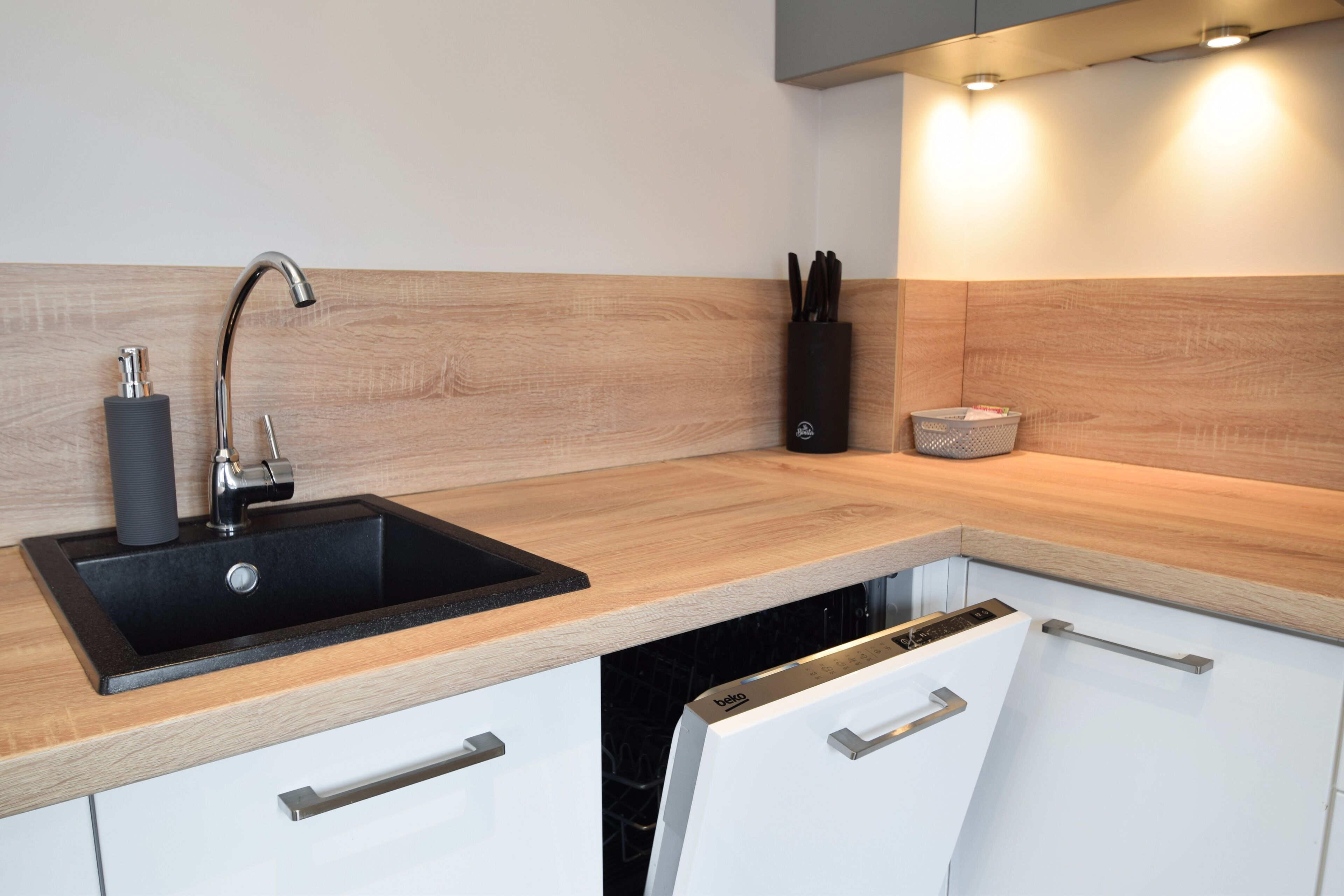 A modern kitchen with a black sink, wooden countertop, white cabinets, and a dish rack.