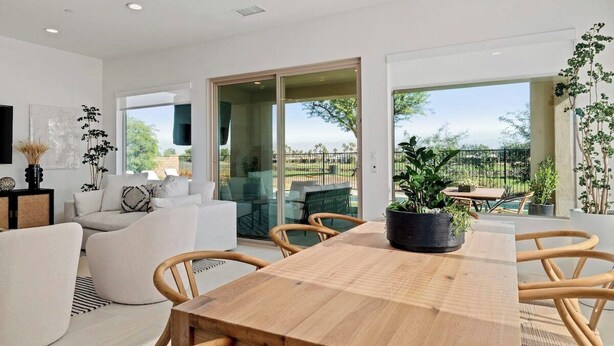 Una sala de estar moderna con una mesa de comedor de madera, sofás blancos y un amplio ventanal corredero que da a un patio exterior.