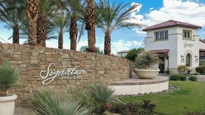 Un muro de piedra con el texto “Signature at PGA WEST” y un edificio con tejado de tejas rojas.