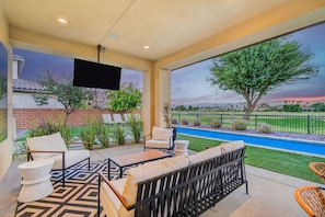 An outdoor patio with a pool, seating area, and a large TV screen.