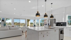 Una cocina moderna con una isla grande, armarios blancos e iluminación colgante.