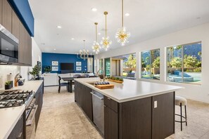 A modern kitchen with a large island, dark cabinetry, and pendant lighting. - Poolside Paradise | Fire Pit & Golf Next Door (La Quinta)
